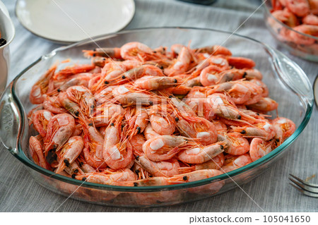 A dish of unpeeled shrimp on a dinner table with plates. Seafood diner. Boiled shrimps. 105041650