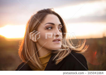 Young beautiful woman enjoying nature while standing in autumn field at sunset 105041864