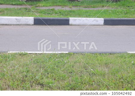 A street border painted in white and black on the background of the road and green foliage.  safety 105042492