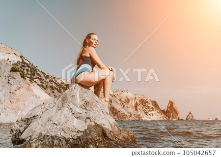Woman travel summer sea. A happy tourist in a blue bikini enjoying the scenic view of the sea and volcanic mountains while taking pictures to capture the memories of her travel adventure. 105042657