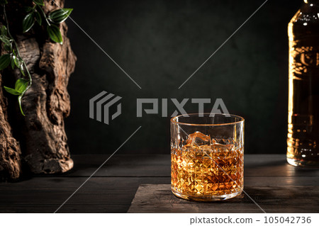 Glass of whisky with ice and bottle on wooden table on dark background with copy space. Glass of whisky with ice and bottle on wooden table on dark background with copy space. 105042736