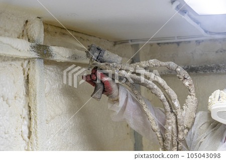 worker in a protective suit insulates the walls with polyurethane foam 105043098