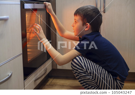A child is sitting near the oven in the kitchen and waiting. A child is sitting near the oven in the kitchen and waiting. 105043247
