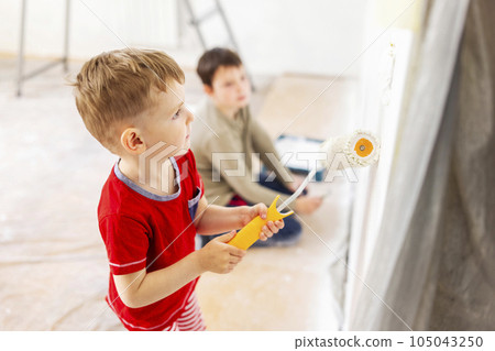 Children paint a wall with brush and roller in white color. Children paint wall Children paint a wall with brush and roller in white color. Children paint wall 105043250
