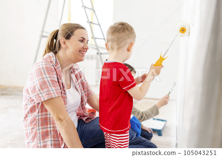 Mother with her children painting the wall with paint using roller and brush 105043251