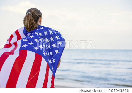 Back view of young woman holding national American flag on a ocean beach Back view of young woman holding national American flag on a ocean beach 105043266