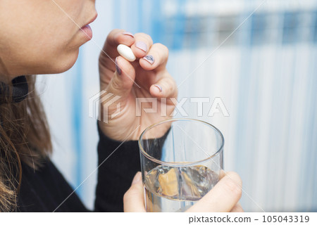 Females hands are holding one tablet and glass of water close up Females hands are holding one tablet and glass of water close up 105043319
