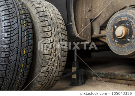 Car on tire mounting with removed wheel on pneumatic jack. Seasonal tire change 105043339