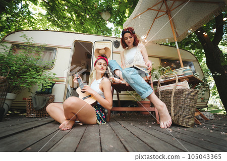 Happy hippie friends are having a good time together with guitar in camper trailer. Holiday, vacation, trip concept. Happy hippie friends are having a good time together with guitar in camper trailer. Holiday, vacation, trip concept. 105043365