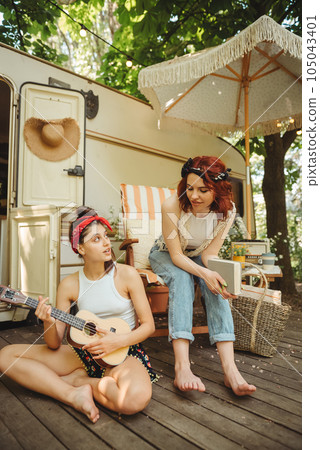 Happy hippie girls are having a good time with playing on guitar in camper trailer. Holiday, vacation, trip concept. Happy hippie girls are having a good time with playing on guitar in camper trailer. Holiday, vacation, trip concept. 105043401