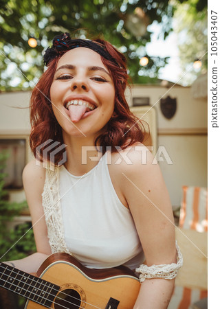 Happy hippie girl is having a good time with playing on guitar in camper trailer. Holiday, vacation, trip concept. 105043407