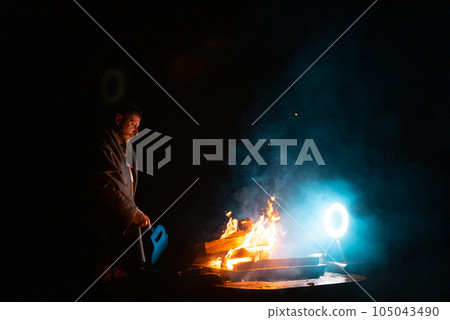Man preparing bbq grill to cook on fire. Outside dark shot. Freeze moment of fire Man preparing bbq grill to cook on fire. Outside dark shot. Freeze moment of fire 105043490