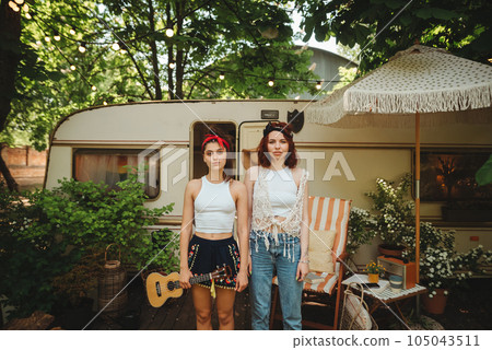 Happy hippie girls are having a good time with playing on guitar in camper trailer. Holiday, vacation, trip concept. 105043511