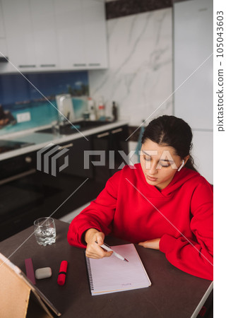 Beautiful girl with headphones is holding a pen in her hand and writing information from tablet to a notebook 105043603