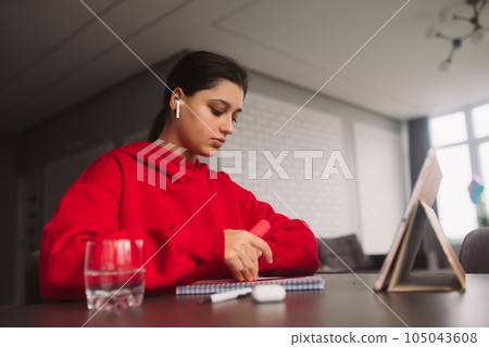Beautiful girl with headphones is holding a marker and line in her hand and writing information from tablet to a notebook Beautiful girl with headphones is holding a marker and line in her hand and writing information from tablet to a notebook 105043608