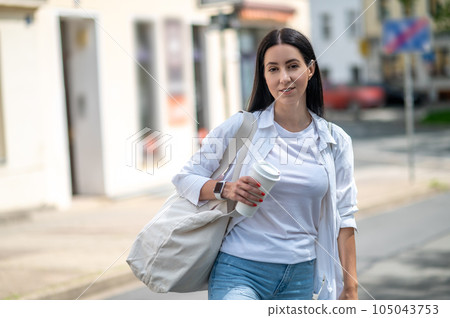 Young woman walking on the street, wearing casual clothing, holding bag. Young woman walking on the street, wearing casual clothing, holding bag. 105043753
