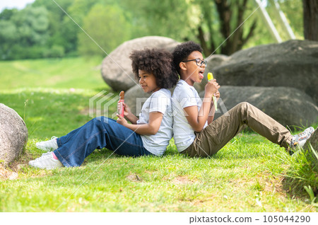 Two children eating ice cream in park sitting on green grass. Two children eating ice cream in park sitting on green grass. 105044290