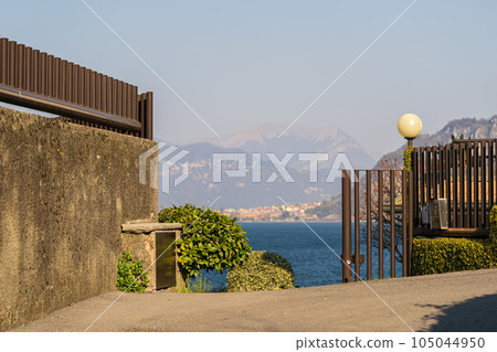 Cement and metal fence with view on mountains and lake, Lombardia 105044950