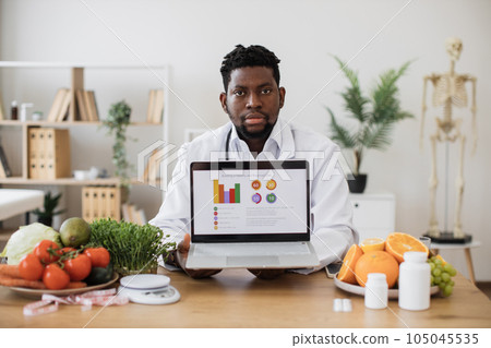 Nutrition specialist posing on camera with portable laptop Nutrition specialist posing on camera with portable laptop 105045535