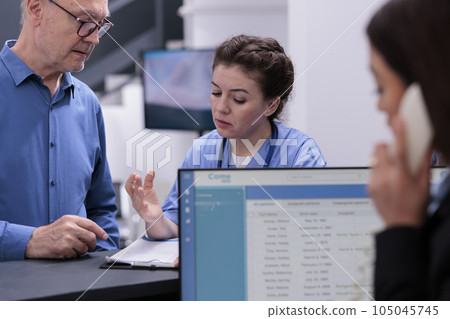 Assistant looking at medical report with old patient while signing documents before start consultation in hospital waiting room. Senior man having checkup visit with medic, health care service Assistant looking at medical report with old patient while signing documents before start consultation in hospital waiting room. Senior man having checkup visit with medic, health care service 105045745