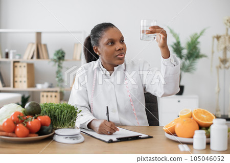 Nutrition specialist checking fluid in glass at workplace Nutrition specialist checking fluid in glass at workplace 105046052