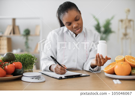 Female with medicine bottle writing on paper in office Female with medicine bottle writing on paper in office 105046067