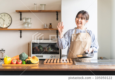 穿著圍裙的婦女/家庭主婦在廚房裡使用煎鍋（微笑/揮手） 105050122