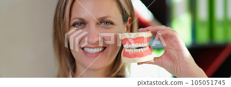 Female dentist smiling and shows artificial jaws in her hand closeup. 105051745