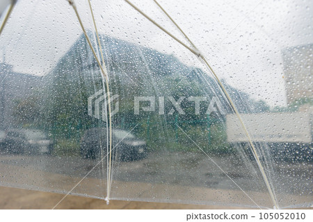 Walking through a deserted unpaved factory town with raindrops on a plastic umbrella 105052010