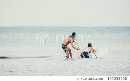 Sea woman and man on sup. Silhouette of happy young woman and man, surfing on SUP board, confident paddling through water surface. Idyllic sunset. Active lifestyle at sea or river. 105053306