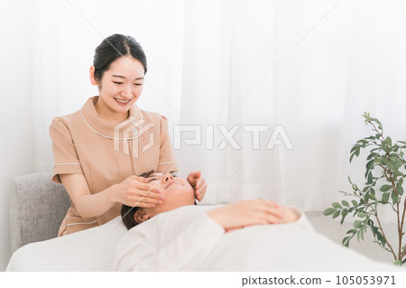 A therapist esthetician and a woman who perform facial esthetics and small face correction at an esthetic salon 105053971