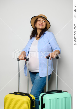 Beautiful pregnant woman travelling abroad, smiles looking aside, poses with suitcases, isolated white studio background Beautiful pregnant woman travelling abroad, smiles looking aside, poses with suitcases, isolated white studio background 105056170