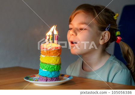Happy little preschool girl celebrating birthday. Closeup of child with homemade rainbow cake, indoor. Happy healthy toddler blowing six candles on cake. Selective focus on cake Happy little preschool girl celebrating birthday. Closeup of child with homemade rainbow cake, indoor. Happy healthy toddler blowing six candles on cake. Selective focus on cake 105056386
