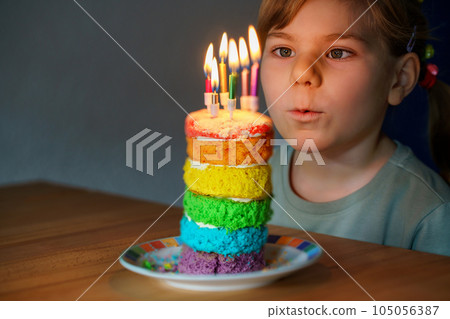Happy little preschool girl celebrating birthday. Closeup of child with homemade rainbow cake, indoor. Happy healthy toddler blowing six candles on cake. Selective focus on cake Happy little preschool girl celebrating birthday. Closeup of child with homemade rainbow cake, indoor. Happy healthy toddler blowing six candles on cake. Selective focus on cake 105056387