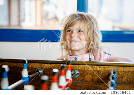 Little preschool girl playing table soccer. Happy excited positive child having fun with family game with siblings or friends. Little preschool girl playing table soccer. Happy excited positive child having fun with family game with siblings or friends. 105056401