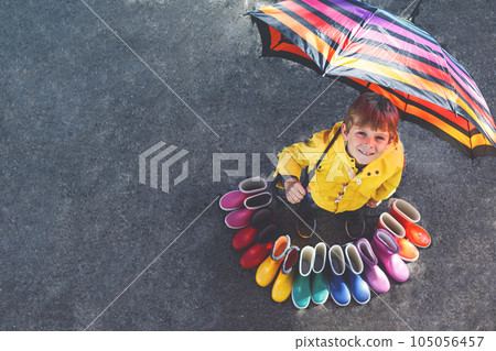 Little kid boy and group of colorful rain boots. Blond child standing under umbrella. Close-up of schoolkid and different rubber boots from high angle. Footwear for rainy fall Little kid boy and group of colorful rain boots. Blond child standing under umbrella. Close-up of schoolkid and different rubber boots from high angle. Footwear for rainy fall 105056457