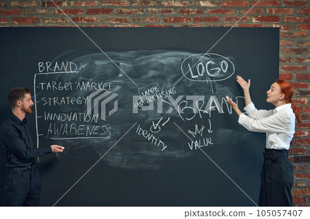 Man and woman, colleagues writing on blackboard marketing strategies of brand development. Building successful business strategies 105057407