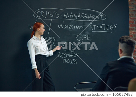 Coworkers meeting together work management strategies discussion. Woman writing plan on blackboard. Business education and skills Coworkers meeting together work management strategies discussion. Woman writing plan on blackboard. Business education and skills 105057492