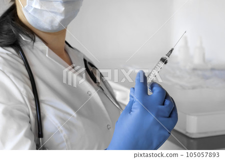 Nurse pushing air out of syringe for vaccine injection. Doctor wearing blue gloves and medical mask. Person holds a syringe with medicine in his hand Close Up. She ready to give an injection. Science Nurse pushing air out of syringe for vaccine injection. Doctor wearing blue gloves and medical mask. Person holds a syringe with medicine in his hand Close Up. She ready to give an injection. Science 105057893