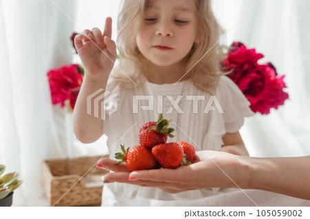 A little blonde girl on a kitchen countertop decorated with peonies. Spring atmosphere. 105059002
