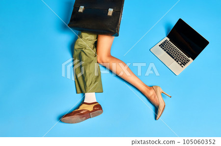 Deadlines. Male and female body parts. Legs in boots and heels with briefcase and laptop against blue studio background Deadlines. Male and female body parts. Legs in boots and heels with briefcase and laptop against blue studio background 105060352