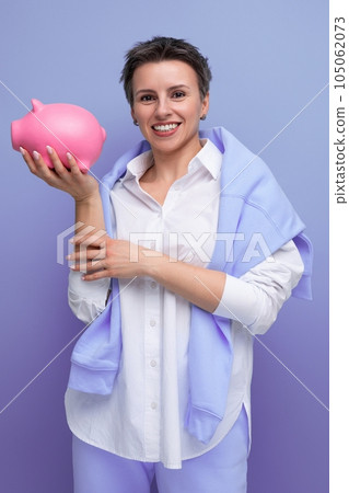 authentic young woman with short haircut keeps her savings in a piggy bank 105062073
