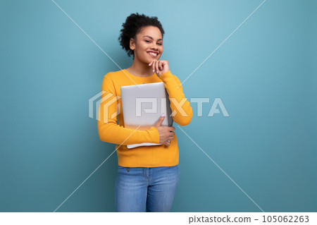 pretty young brunette latin female adult in yellow sweater holding a laptop in her hands pretty young brunette latin female adult in yellow sweater holding a laptop in her hands 105062263