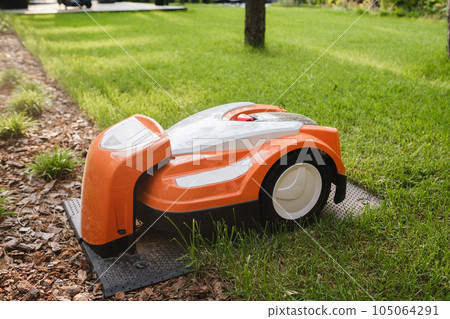 An orange robotic lawn mower stands on the base and is charged from electricity in the courtyard 105064291