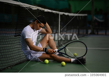 Disappointed asian male tennis player sitting on the court, upset about competition loss, failure emotions Disappointed asian male tennis player sitting on the court, upset about competition loss, failure emotions 105064901