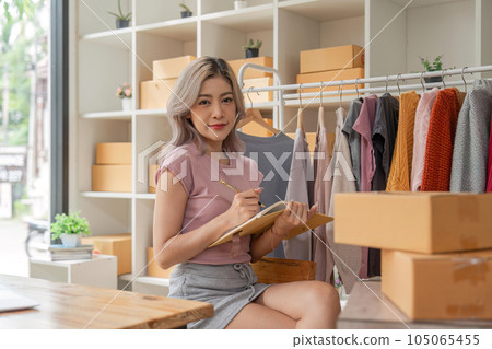 Asian woman entrepreneur of online sell clothing using laptop and taking note in notebook on desk in home office Asian woman entrepreneur of online sell clothing using laptop and taking note in notebook on desk in home office 105065455