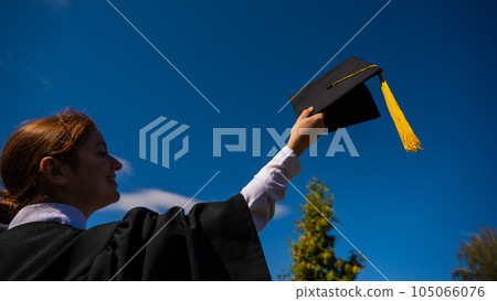 A woman throws her graduation cap against the blue sky. 105066076