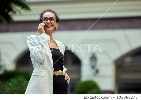 Cheerful, smiling, confident business woman walking outside the office and talking on mobile phone Cheerful, smiling, confident business woman walking outside the office and talking on mobile phone 105068273