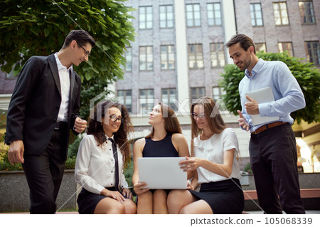 Group of employees, business people, project leaders sitting on bench outside office on daytime and working online on laptop 105068339