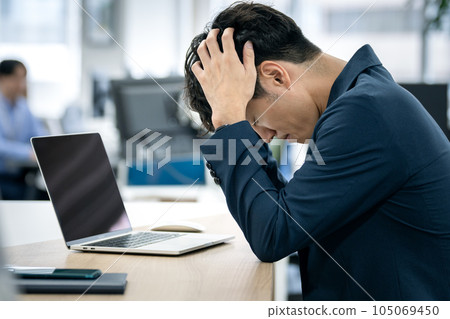 A businessman holding his head in front of a laptop A businessman holding his head in front of a laptop 105069450